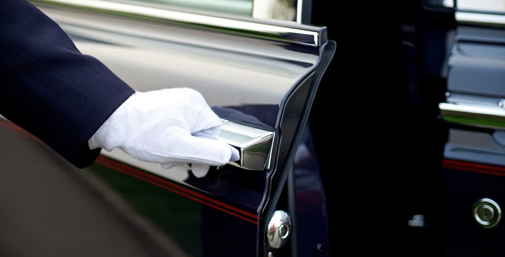 A white-gloved chauffeur's hand resting on the polished chrome handle of a black vehicle door